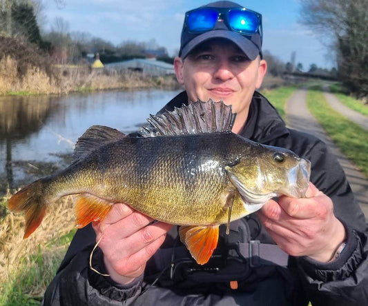picture of a person wearing sunglasses designed for fishing. Holding a perch caught in a canal 
